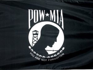 A black and white flag with the silhouette of a prisoner of war (POW) in white, standing in front of a guard tower and barbed wire. Above the figure is "POW" and "MIA" in white on either side of a five-pointed white star. Below the figure, a white wreath encircles the words "You Are Not Forgotten" in black.